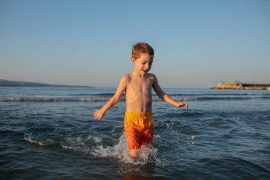 Turuncu şortlu mutlu çocuk yazın sahilde.