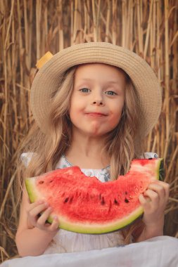 Şapkalı küçük güzel kız yazın buğday tarlasında karpuz yiyor.