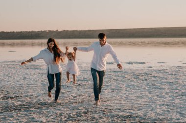Mutlu genç aile: anne, baba ve küçük kızları gün batımında deniz kenarında