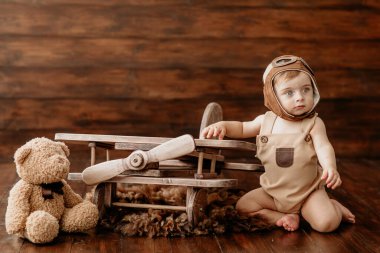 Pilot kıyafetli küçük çocuk ahşap uçağın yanındaki fotoğraf stüdyosunda.