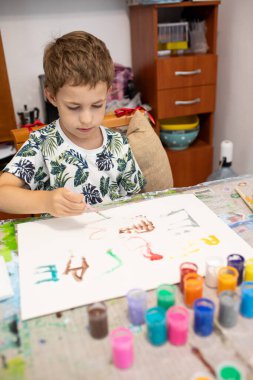 Küçük bir çocuk masada oturur ve resim yapar.