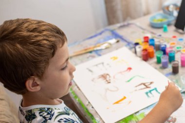 Küçük bir çocuk masada oturur ve resim yapar.