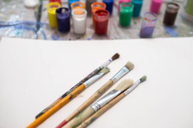 Beyaz bir kağıt üzerinde fırçalar ve masaya çizim yapmak için çok renkli boya kavanozları