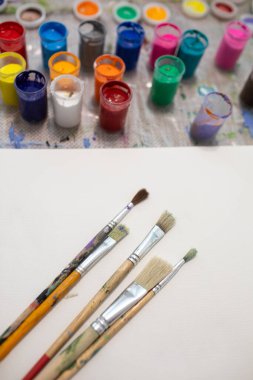 Beyaz bir kağıt üzerinde fırçalar ve masaya çizim yapmak için çok renkli boya kavanozları
