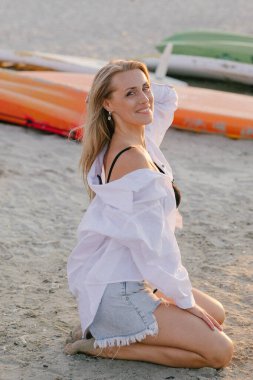 Yazın gün batımında kumsalda, beyaz gömlekli sarışın kız.