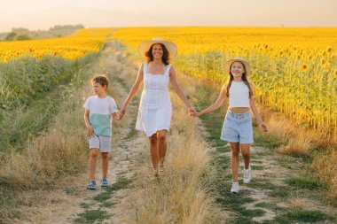 İki çocuklu mutlu bir anne: Oğlu ve kızı yazın günbatımında ayçiçeği tarlasında.