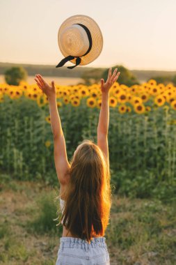 Mutlu kız yazın ayçiçeği tarlasında şapka fırlatır.