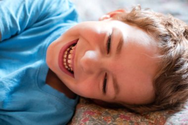 Mavi tişörtlü gülümseyen küçük bir çocuğun portresi.