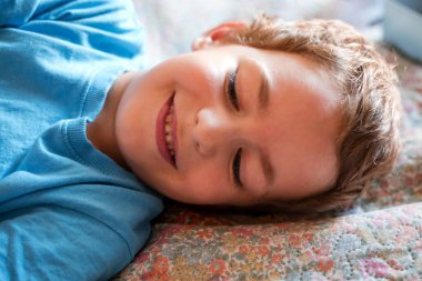 Mavi tişörtlü gülümseyen küçük bir çocuğun portresi.