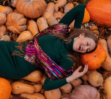 Yeşil kazaklı mutlu kız sonbaharda parktaki balkabağı tepesinde yatıyor. Sonbahar konsepti. Sonbahar sezonu. Cadılar Bayramı