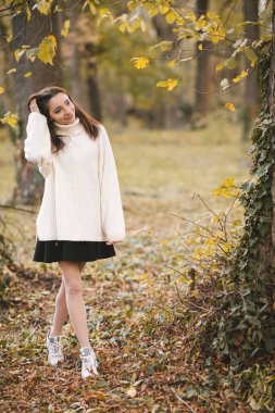 Sonbahar parkında beyaz kazaklı güzel bir genç kız. Sonbahar