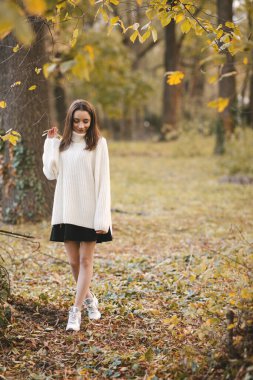 Sonbahar parkında beyaz kazaklı güzel bir genç kız. Sonbahar