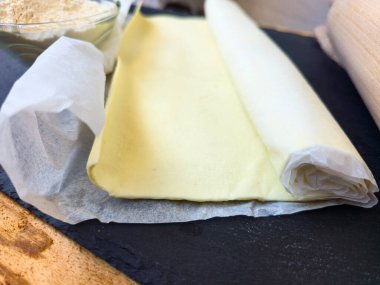 Kara tahtada çiğ puf böreği, yakın plan. Yakınlarda ahşap bir merdane ve un var. Ev yapımı ya da hamur hazırlığı kavramı.