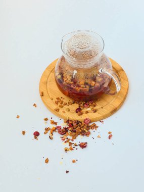 Beyaz zemin üzerinde ahşap bir standın üzerinde meyveli sonbahar çayı ile şeffaf çaydanlık. Sonbahar. Sonbahar havası. konfor