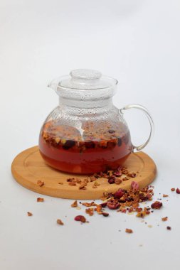 Beyaz zemin üzerinde ahşap bir standın üzerinde meyveli sonbahar çayı ile şeffaf çaydanlık. Sonbahar. Sonbahar havası. konfor