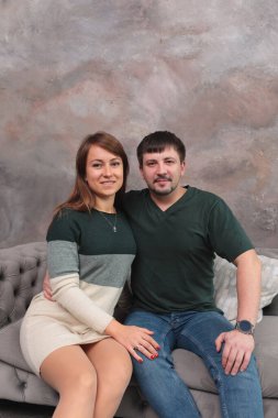 Gri bir duvara karşı gri bir kanepede oturan güzel genç kız.