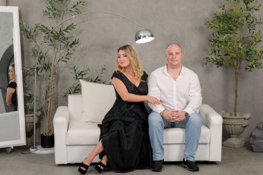 Beyaz bir kanepede gri bir duvara yaslanmış birbirini seven bir çift. Karı koca. damat ve gelin