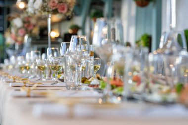 Bardaklar masaya. Düğün masası. Lüks bir düğün için uzun bir ziyafet masasında zarif şarap kadehlerinin yakın plan çekimi ya da sığ bir tarla derinliği olan güzel bir yemek etkinliği.