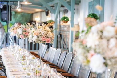 wedding table decoration.  elegant long banquet table set for a wedding reception indoors, decorated with luxurious floral centerpieces in pastel pink and blush tones