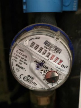 Close-up of a modern residential digital water meter with a roller counter, showing a specific reading of water consumption, installed on a dark pipeline