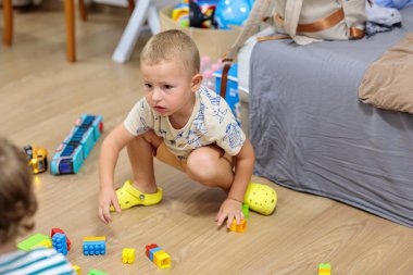 little boy playing with toys.  A focused young boy sits on a floor in a casual home setting, intently stacking colorful plastic construction blocks to build a tower, illustrating imaginative play