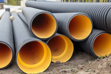 Black corrugated plastic drainage pipes with bright yellow interior stacked outdoors on a construction site for sewage, storm water, or cable protection