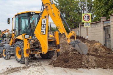 Rear view of a yellow JCB backhoe loader with a digging bucket working on a large pile of dirt and soil at a construction site.  