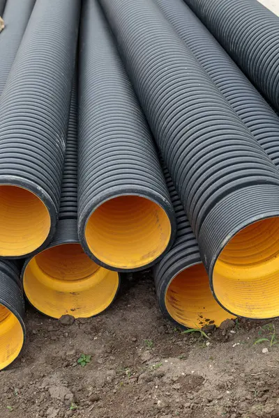 Black corrugated plastic drainage pipes with bright yellow interior stacked outdoors on a construction site for sewage, storm water, or cable protection
