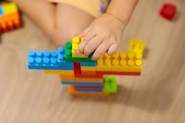 child playing with blocks.  Child's hands building a colorful plastic block tower on the wooden floor