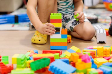 child playing with blocks.  Child's hands building a colorful plastic block tower on the wooden floor