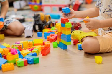 child playing with blocks.  Child's hands building a colorful plastic block tower on the wooden floor