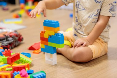 child playing with blocks.  Child's hands building a colorful plastic block tower on the wooden floor