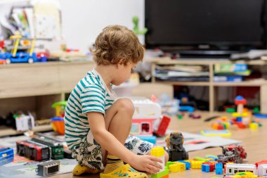 Little boy playing with colorful plastic building blocks on the floor