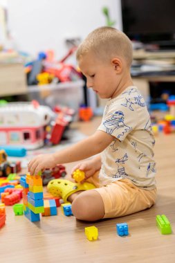Little boy playing with colorful plastic building blocks on the floor