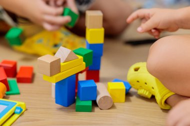 child playing with blocks.  Close-up of children's hands building tall tower with colorful wooden blocks on floor