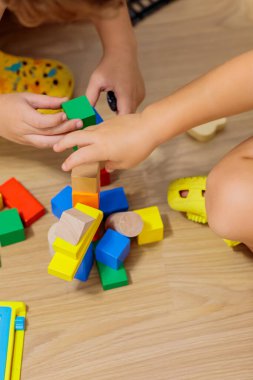 child playing with blocks.  Close-up of children's hands building tall tower with colorful wooden blocks on floor