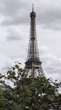 Ön planda, yapraklar hafif bir esintide sallanıyor. Arka planda, dünyaca ünlü Eyfel Kulesi bulutlu bir gökyüzüne karşı görkemli bir şekilde duruyor. Paris, Fransa 'daki Seine Nehri' nin sağ kıyısından çekilmiştir..