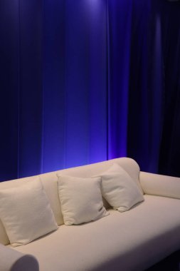 Derin mavi perde duvarına dayalı beyaz modern kanepe, şık ve minimal iç dekorasyon.