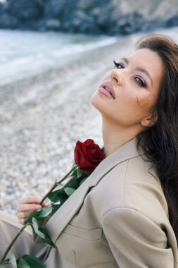Elinde kırmızı gül olan bej ceketli güzel bir kadının portresi.