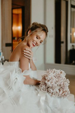 Gelin elinde bir buket çiçek tutarken lüks otel odasında kötülerin üzerine oturuyor. 