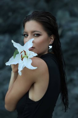 Siyah kayalıklarda beyaz Lilly ile genç bir kadının portresi. 