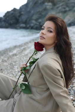 Kumsalda oturan ve bej takım elbiseli bir kız. 