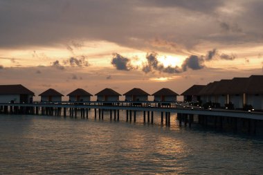 Güzel tropikal gün batımı gökyüzü. Gün batımı, deniz aşırı bir bungalovdan gelen sakin suları yansıtıyor. Sakin ve romantik tropikal akşam sahnesi.