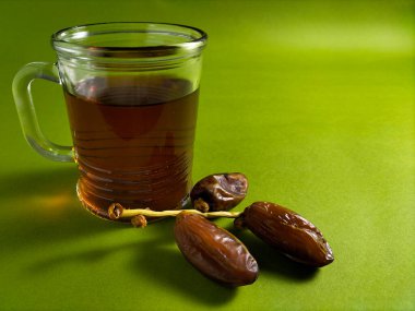 a glass of tea with dried dates fruits on green