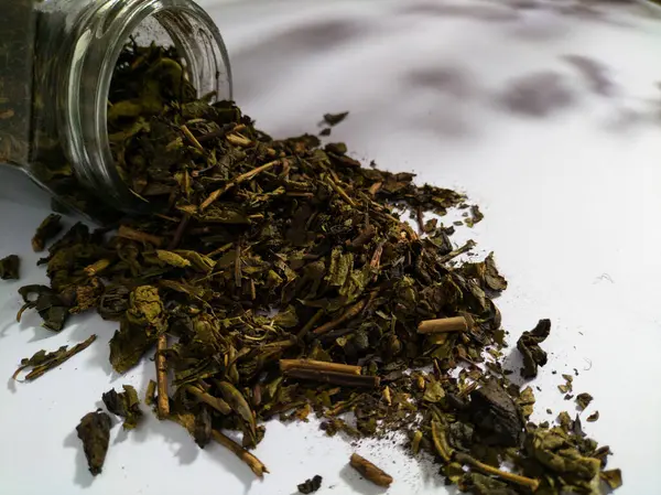 Şeffaf cam bir kavanozdan beyaz bir yüzeye dökülen kurumuş çay yaprakları.