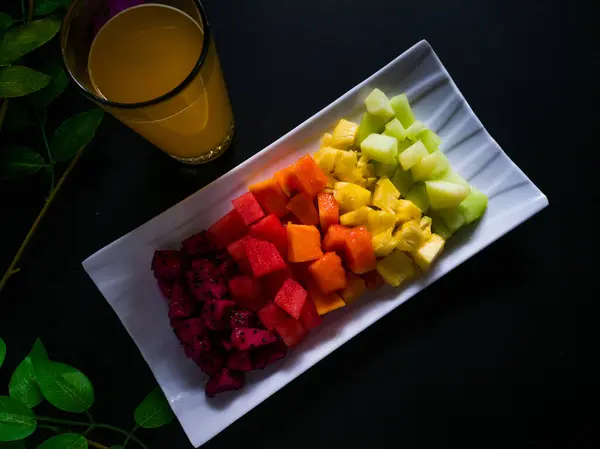 Siyah arkaplanda meyve salatası olan dikdörtgen bir tabak.