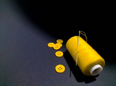 Sarı iplikli bir makara iğne ve koyu arkaplan üzerinde sarı düğmeler.