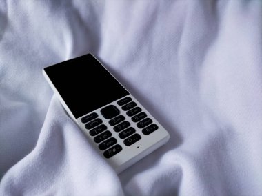 Beyaz kumaşta eski bir cep telefonu.