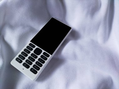 Beyaz kumaşta eski bir cep telefonu.