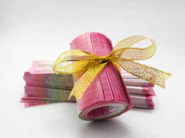 Beyaz arka planda altın kurdeleli düzgünce yuvarlanmış banknotlar.